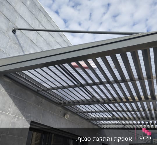 פרגולה מתכתית עם גג שקוף על קיר חיצוני